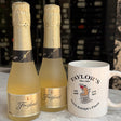 Two bottles of Freyconet sparkling wine and a white ceramic mug printed with 'Taylor's Since 1980' and a cartoon bear, set on a white marble surface with a dark wine cellar background.